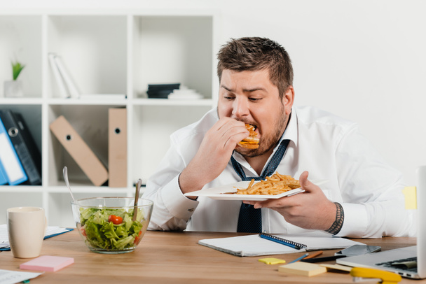 homme d'affaires en surpoids manger un hamburger tout en regardant la salade
 - Photo, image