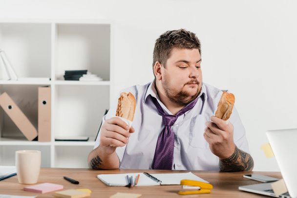 nadwagą biznesmen jedzenie hotdogs w miejscu pracy w biurze - Zdjęcie, obraz
