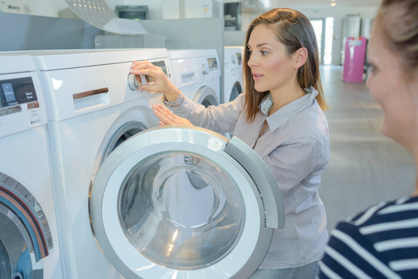 Woman demonstrating washing machine to customer - Zdjęcie, obraz