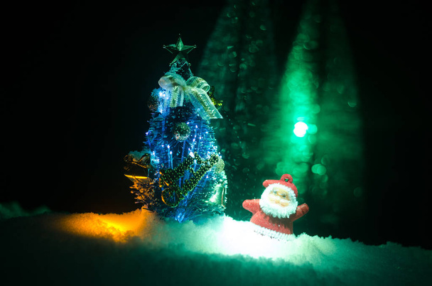 Feliz muñeco de Papá Noel en Navidad con árbol y nieve. Fondo bokeh colorido. Santa Claus y Feliz Navidad modelo figura juguete en tono oscuro
 - Foto, imagen