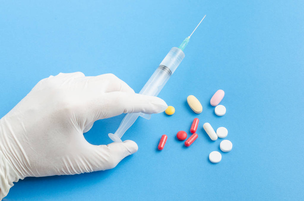 The hand of the medical worker in white gloves, holding a syringe on a blue background and tablets - Foto, imagen