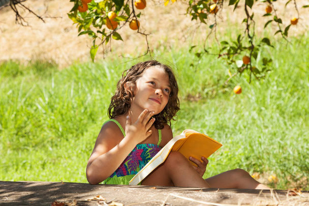 a beautiful little girl reading a yellow book in the garden with - Фото, зображення