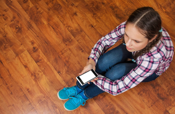 menina de jeans senta-se no chão de madeira e segurando um smartphone. Conceito de vida adolescente e gadgets. Vista superior com espaço de cópia
. - Foto, Imagem