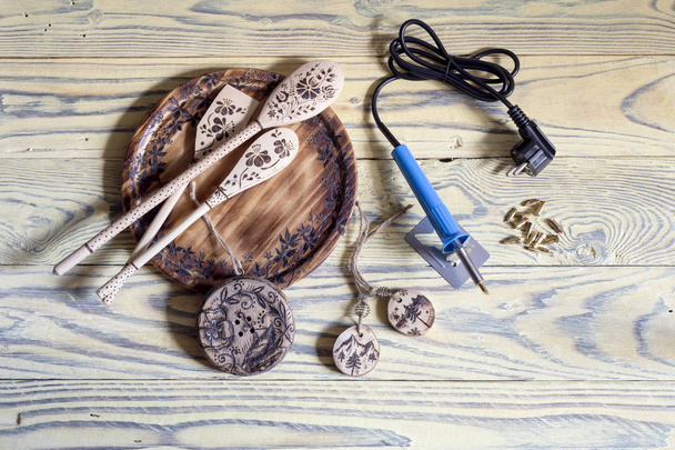 Um conjunto de ferramentas para queimar madeira com bicos e exemplos de objetos de madeira com desenhos em uma mesa de madeira close-up
 - Foto, Imagem