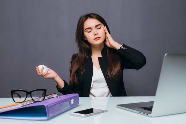 Młoda kobieta interesu dmuchanie jej nos z przodu o biurko komputerowe z bólem głowy - Zdjęcie, obraz