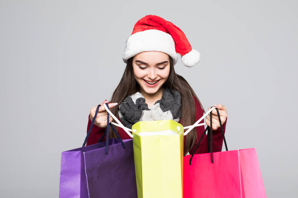 Young pretty woman in santa hat with shopping bags on grey background - Zdjęcie, obraz