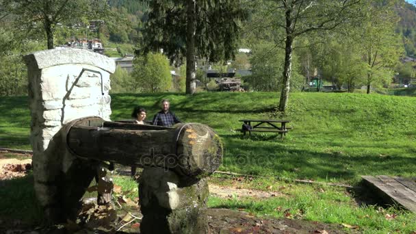 Couple hiking with poles in wood and drinking water on the fountain. Fall time. Hikers trekking in a field near picnic area, tourists walking outdoor and sport in contact with nature - Footage, Video
