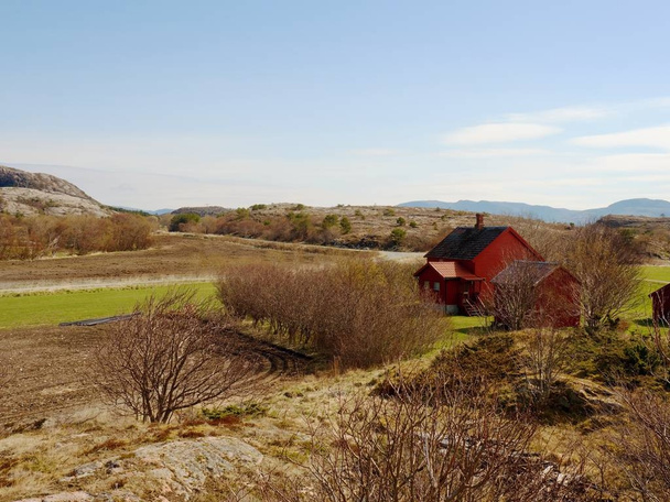 Una cabaña tradicional de madera roja casa abajo colina rocosa. Casa en diseño clásico de Noruega
 - Foto, Imagen