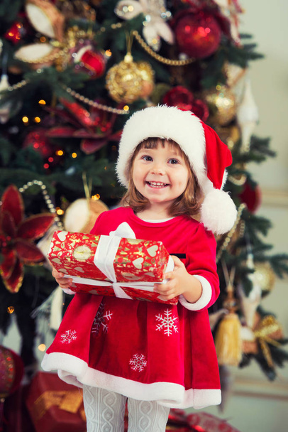 Happy girl with a gift in hands on a background of a New Year tree. - Foto, afbeelding