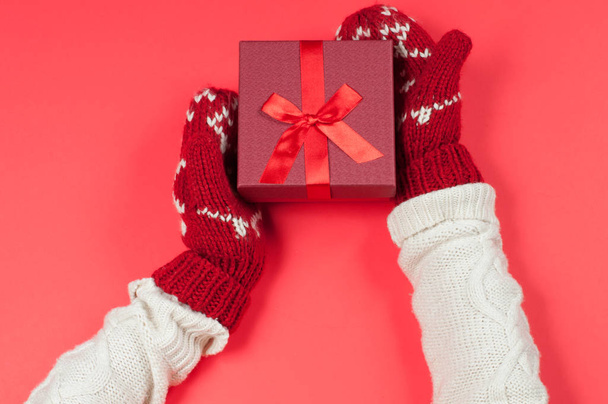 Female hands holding christmas gift in red mittens - 写真・画像