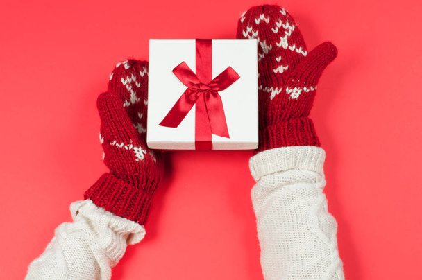 Female hands holding christmas gift in red mittens - Fotoğraf, Görsel
