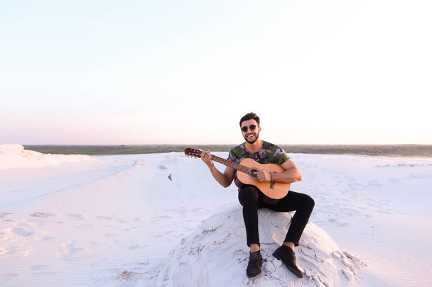 Cute young male Arab enjoys sound of guitar, sitting on hill in - Photo, image