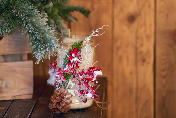 White candle holder decorated with pine cone and red ashberry under Christmas tree on wooden background - Photo, image