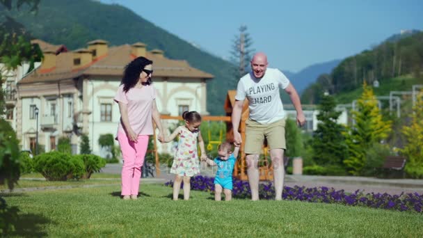 Giovane famiglia caucasica spensierata corre felicemente lungo l'erba verde tenendosi per mano, volti felici della famiglia
. - Filmati, video