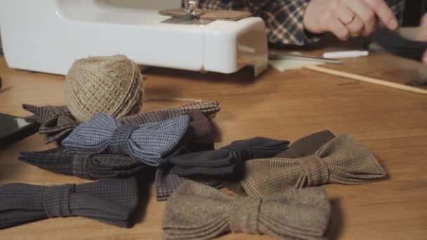 veel van het klaar gemaakte vlinder strikjes gemaakt van wol op de voorgrond, voegt een afgewerkt product. Goed uitziende jonge man werken als een kleermaker en een naaimachine gebruiken in een textiel-studio. - Video