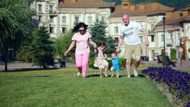 Jeune famille caucasienne insouciante court joyeusement le long de l'herbe verte tenant la main, visages heureux de la famille
. - Séquence, vidéo