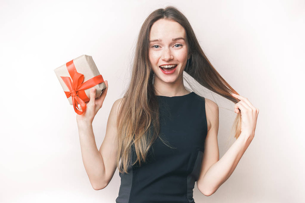 Funny woman got gift. beautiful girl in black dress holds a gift in hands - Foto, imagen