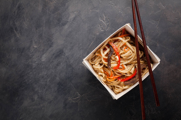 Close-up van de noedels in een doos met groenten en rundvlees in teriyaki saus. Bovenaanzicht van Aziatisch eten en houten stokken. Het concept van fast food. Kopiëren van ruimte - Foto, afbeelding