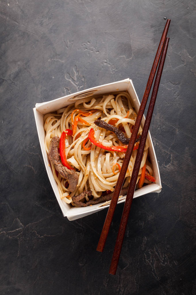Közeli kép: egy doboz zöldség tészta és a marhahús teriyaki szósz. Felülnézet, ázsiai étel, és a fából készült botok. A fogalom fast food - Fotó, kép