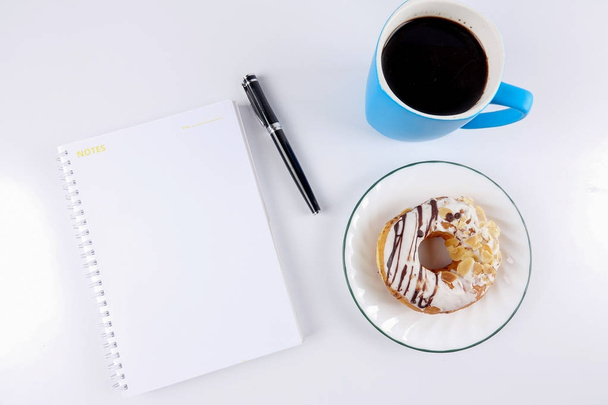 Geopend van Kladblok en kopje koffie met de donut op de witte tafel - Foto, afbeelding