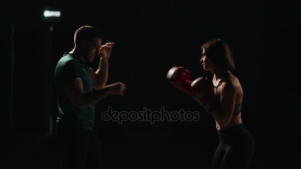 Dívka svalová fitness trénink s jeho instruktor provádět údery na nohy v Boxerské rukavice. Lekce sebeobrany. Trénink boxu. - Záběry, video