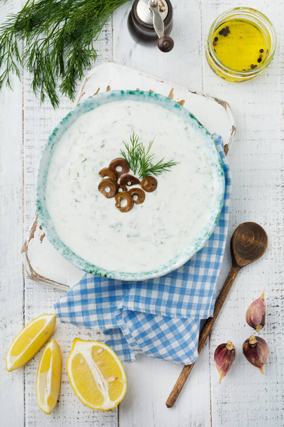 Traditional Greek sauce Tzatziki. Yogurt, cucumber, dill, garlic and salt oil in a ceramic bowl on a light wooden background. Rustic style. Selective focus. Top view. - Valokuva, kuva