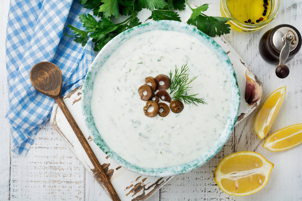 Traditional Greek sauce Tzatziki. Yogurt, cucumber, dill, garlic and salt oil in a ceramic bowl on a light wooden background. Rustic style. Selective focus. Top view. - Photo, image