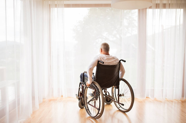 Старший мужчина сидит дома на инвалидной коляске
. - Фото, изображение