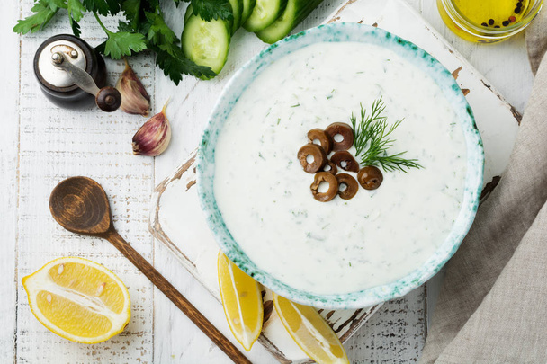 Traditional Greek sauce Tzatziki. Yogurt, cucumber, dill, garlic and salt oil in a ceramic bowl on a light wooden background. Rustic style. Selective focus. Top view. - Фото, изображение