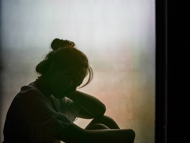 Vintage gefilterd op silhouet van depressief meisje zittend op het venster - Foto, afbeelding