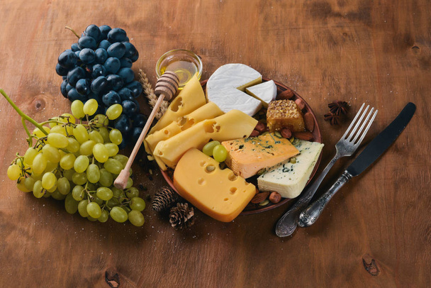 A bottle of wine, and a large assortment of cheeses, honey, nuts and spices, on a wooden table. Top view. Free space for text. - Фото, изображение