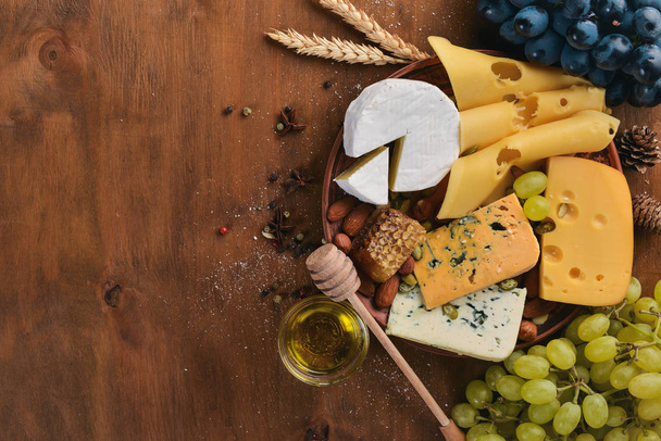 A bottle of wine, and a large assortment of cheeses, honey, nuts and spices, on a wooden table. Top view. Free space for text. - Foto, Imagem