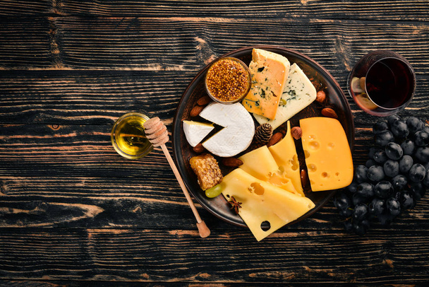 A large assortment of cheeses, brie cheese, gorgonzola, blue cheese, grapes, honey, nuts, red and white wine, on a wooden table. Top view. Free space for text. - Photo, image