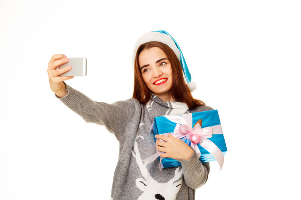 Young happy woman in  warm sweater taking her selfie over white  - 写真・画像