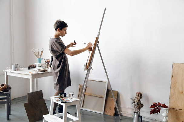 Female artist in her spacious white studio working with watercolor painting.  Natural lighting. Disclosure of creativity concept. Horizontal composition. - Foto, afbeelding