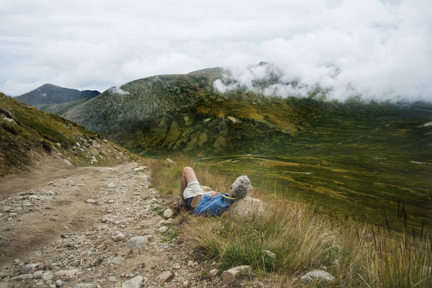 gray-haired senior Man lying down on big stone under heaven with flying clouds. - Foto, afbeelding