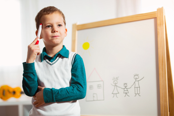 Портрет задумчивого маленького мальчика, рисующего на белой доске войлочной ручкой. Концепция раннего образования
 - Фото, изображение