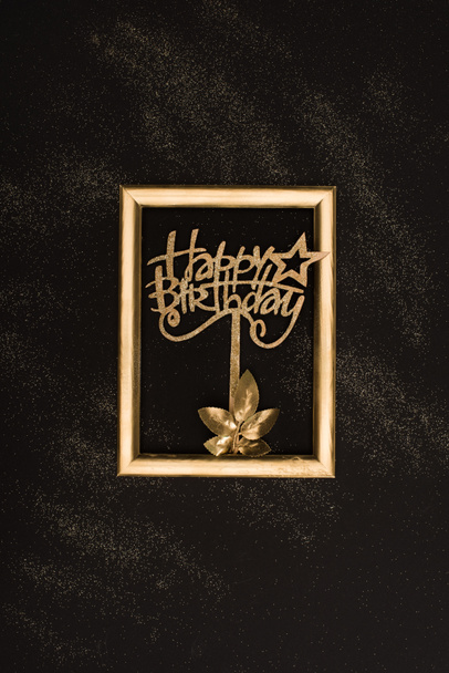 top view of golden happy birthday sign, plant and photo frame on black surface - Фото, зображення
