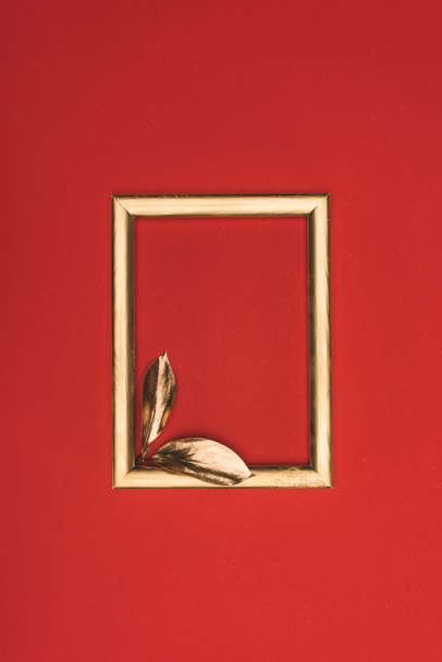 top view of golden photo frame and small leaves isolated on red - Photo, Image