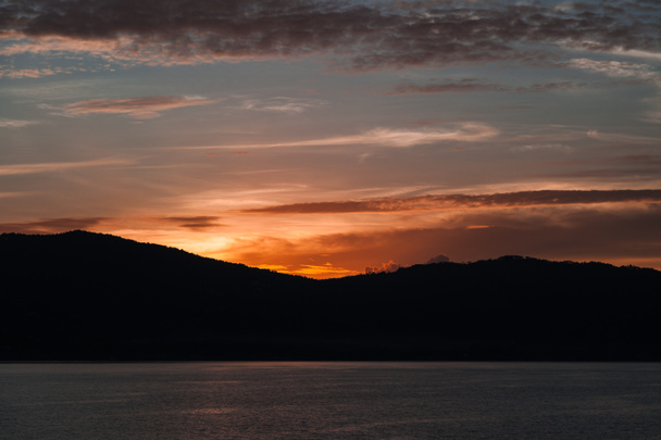 piękny zachód słońca nad sylwetka wzgórza i powierzchni wody - Zdjęcie, obraz