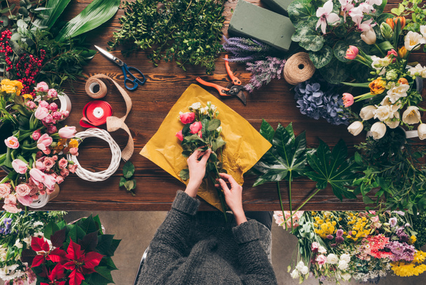 cropped image of female florist wrapping bouquet in pack paper - Photo, Image