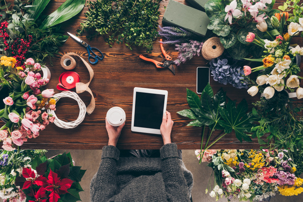cropped image of florist holding coffee in paper cup and tablet in hands - Фото, зображення