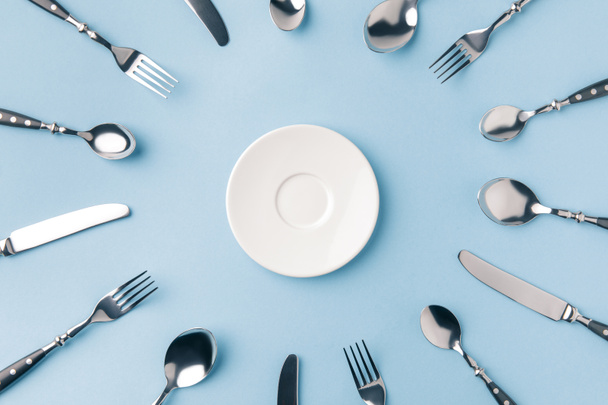 top view of plate surrounded by flatware isolated on blue - Fotografie, Obrázek