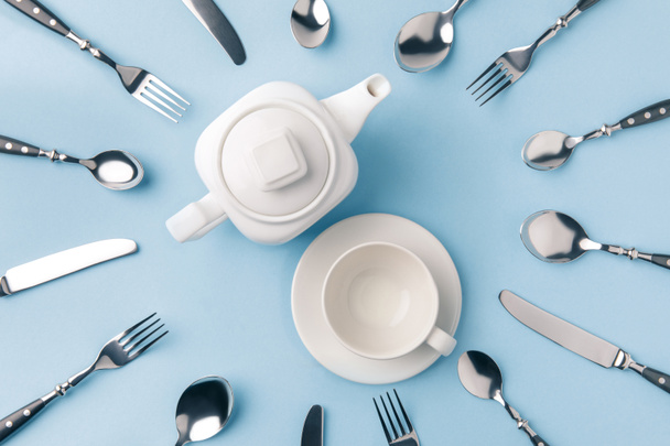 top view of teapot with cup on plate, surrounded by flatware isolated on blue - Foto, immagini