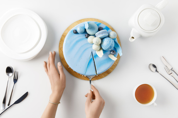 Draufsicht der abgeschnittenen Hände beim Aufschneiden von Kuchen auf Schneidebrett isoliert auf Weiß - Foto, Bild