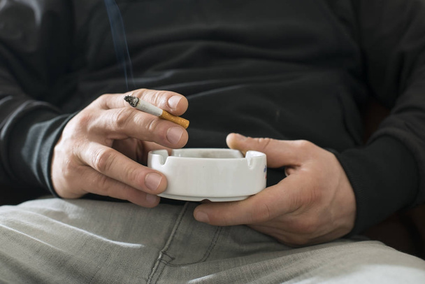 Man holding a cigarette and ashtray - Fotoğraf, Görsel