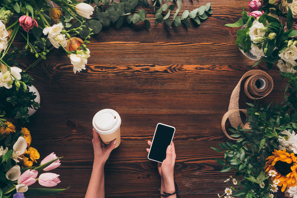 abgeschnittenes Bild eines Blumenhändlers mit Kaffee in Pappbecher und Smartphone in der Hand  - Foto, Bild
