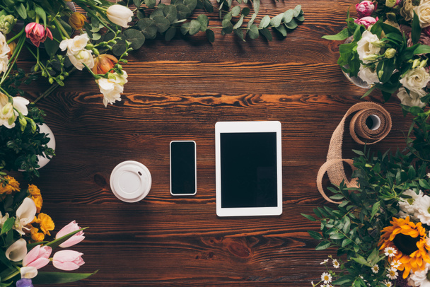 pohled shora kávy v pohárek, smartphone a tablet na stole s květinami - Fotografie, Obrázek