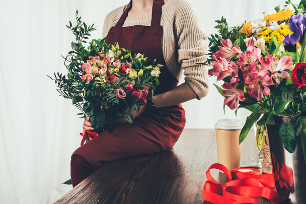 cropped image of florist sitting on table and holding bouquet in hands - Foto, Imagem