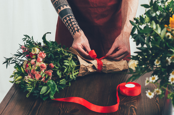 imagen recortada de floristería tatuada masculina atando cinta en ramo
 - Foto, Imagen
